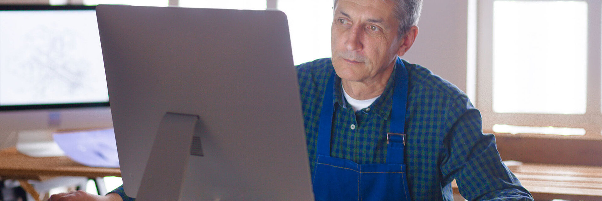 Mann in blauer Latzhose sitzt vor einem Computer